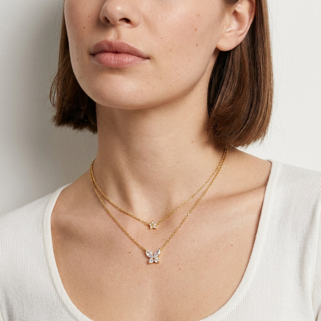 A close-up of a woman wearing a delicate double-layered gold necklace with a butterfly pendant and a small star charm, paired with a white ribbed top.