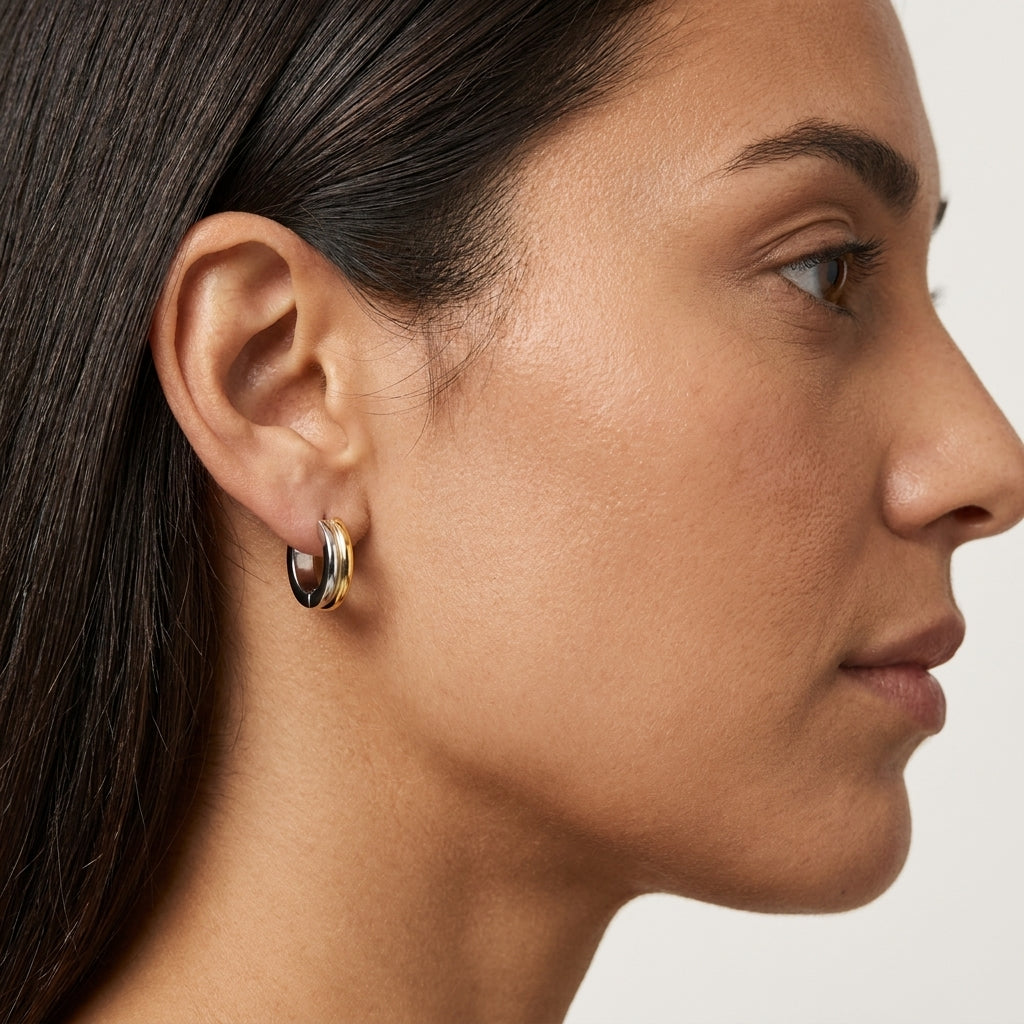 A close-up side profile of a woman wearing a small gold hoop earring with a dark inlay on her earlobe, against a clean light background.