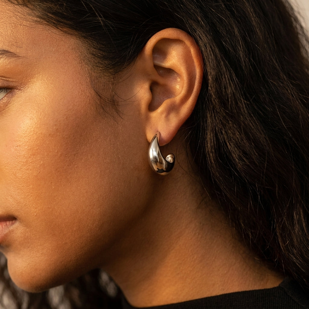 A close-up side profile of a woman wearing a polished silver crescent-shaped hoop earring.