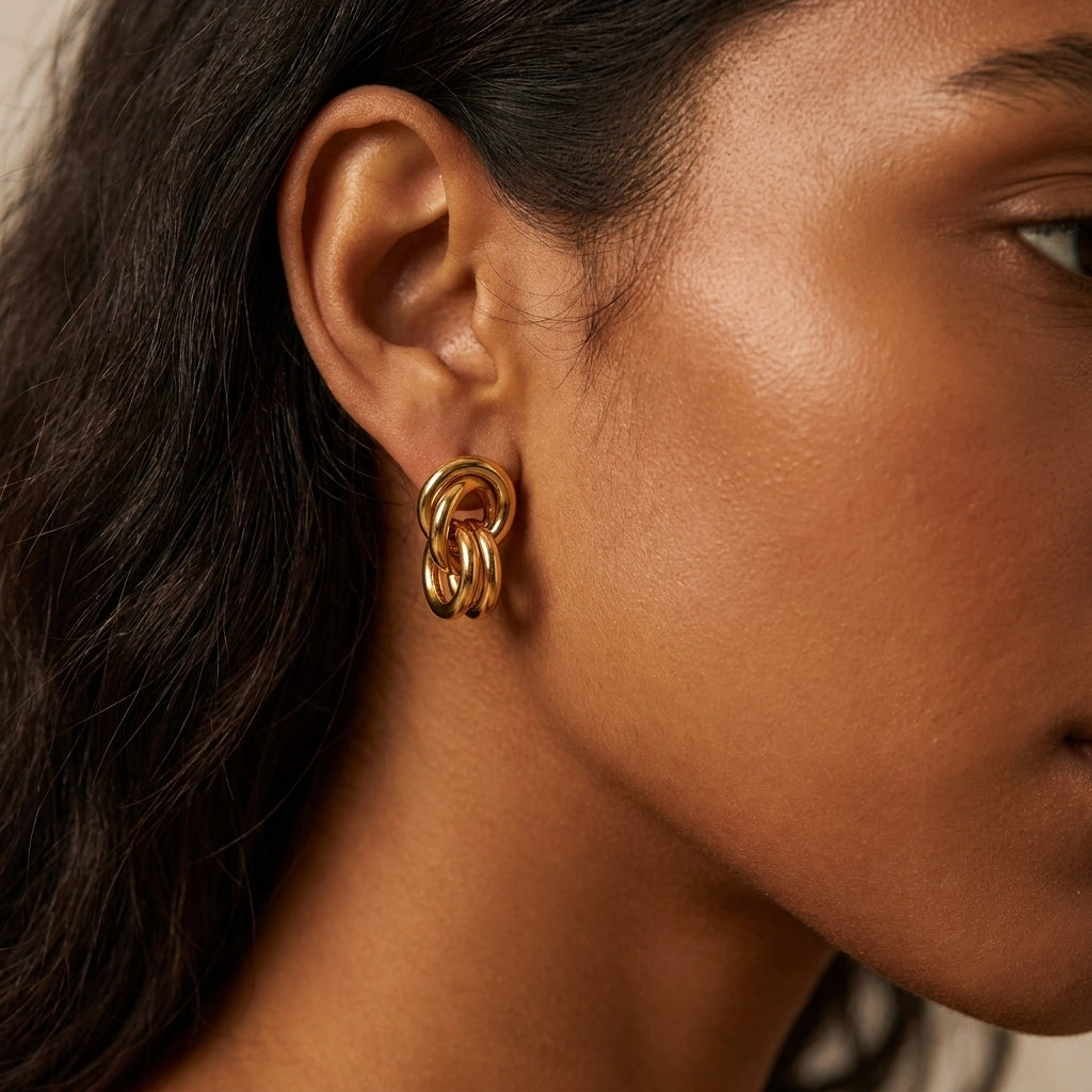 A close-up of a woman's ear wearing a gold triple-ring hoop earring, with her face and dark hair partially visible against a soft neutral background.