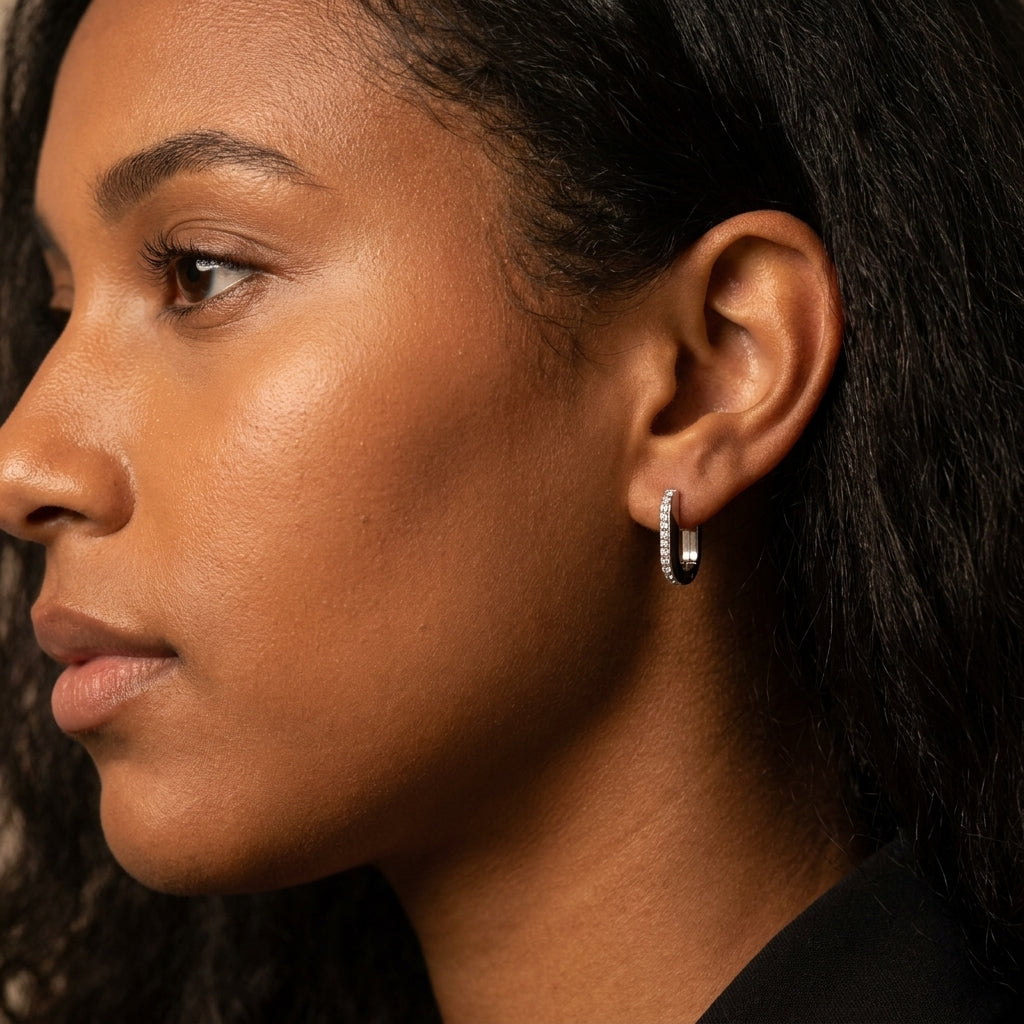 A close-up side profile of a woman wearing a small silver hoop earring with a row of clear stones, set against a dark background.