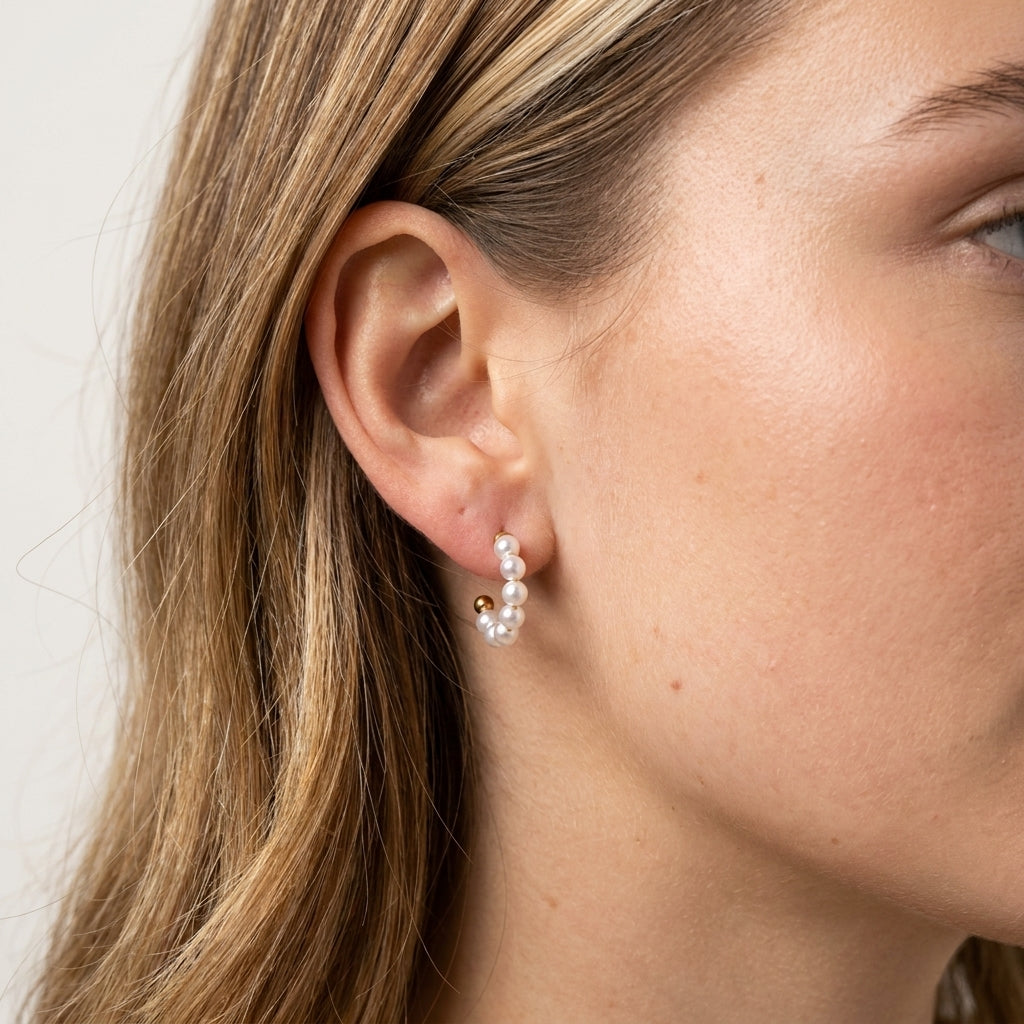 A close-up of a woman's ear wearing a small gold hoop earring adorned with white pearls.
