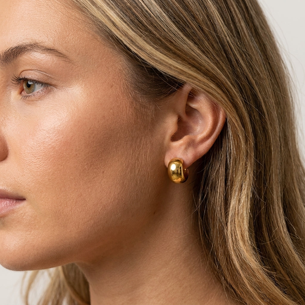 A close-up side profile of a woman wearing a small, polished gold stud earring.
