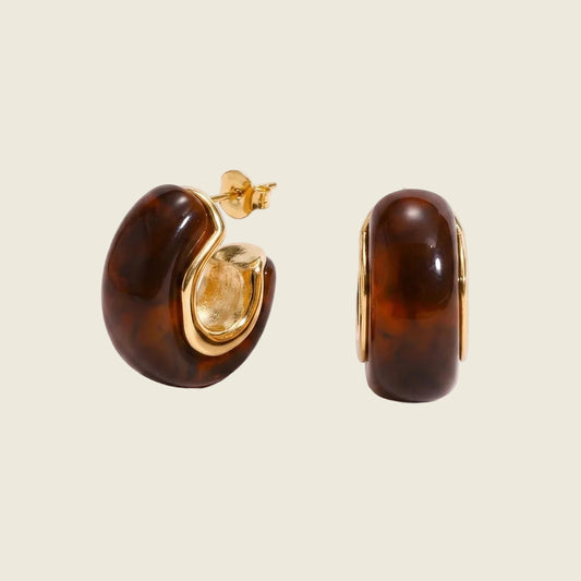 A pair of gold hoop earrings with large, glossy brown marbled resin inlays, shown from both front and side angles on a light pink background.