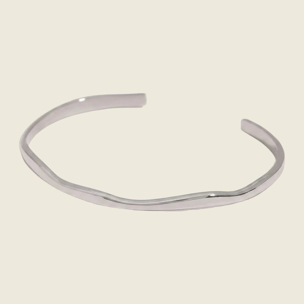 A polished silver-toned metal cuff bracelet with a wavy, organic contour, displayed on a clean white background.