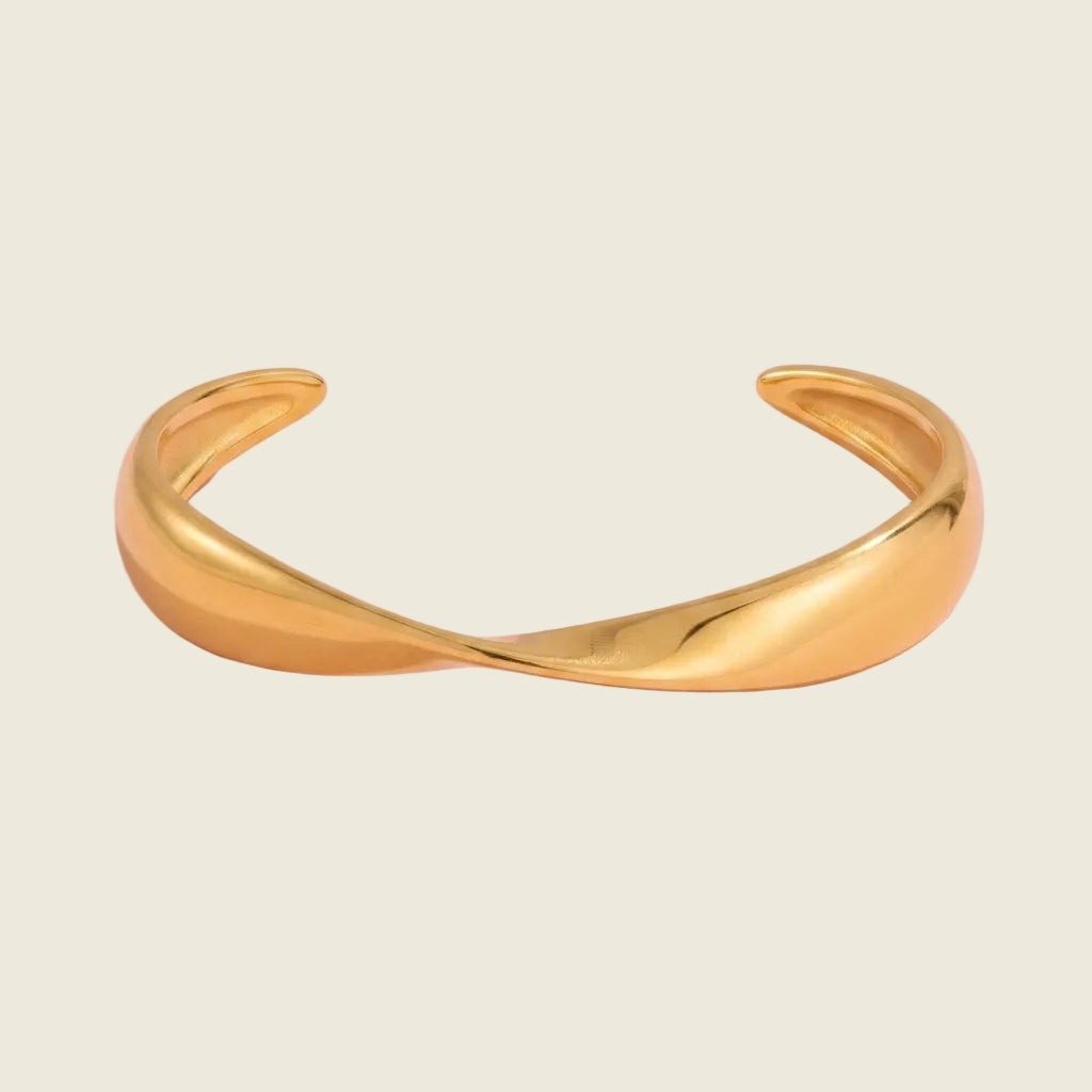 A polished gold-tone twisted cuff bracelet on a solid light pink background.