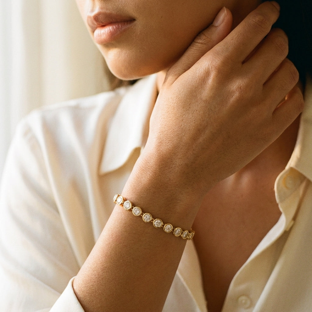 A close-up lifestyle shot of a woman wearing a delicate gold bracelet with round clear stones on her wrist, paired with a cream-colored collared shirt.