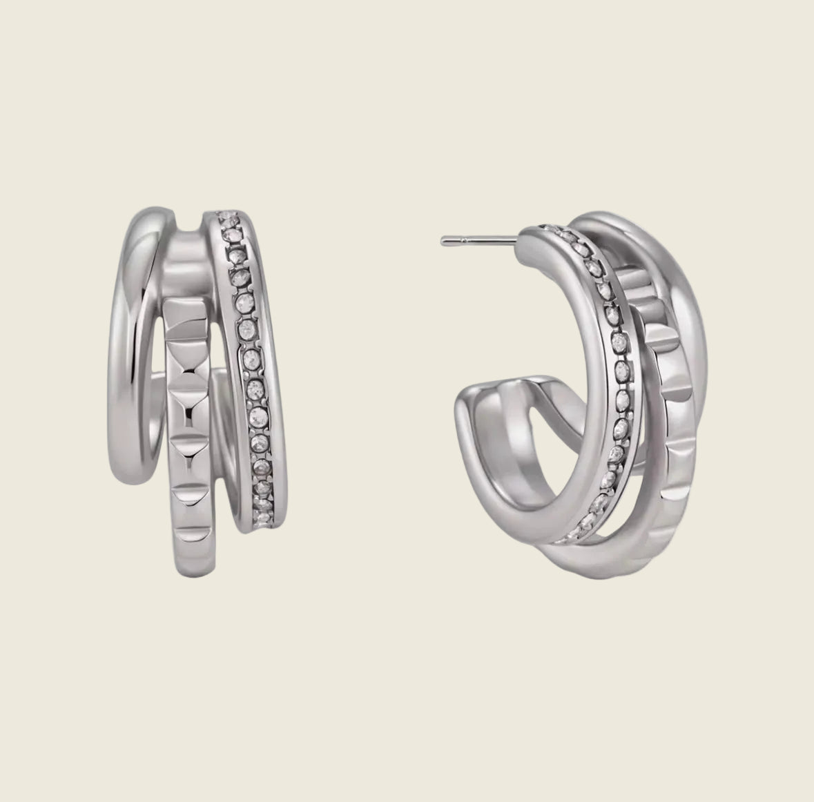 A pair of silver-toned hoop earrings with multiple stacked bands, including one band set with small clear stones, shown on a white background with a soft reflection.