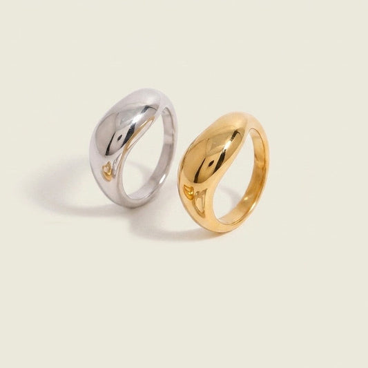 Two polished abstract-shaped rings, one in silver and one in yellow gold, displayed on a light cream background.